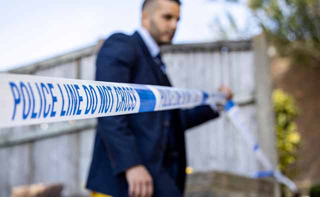 Police detective standing beside police tape.