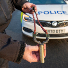 An officer holding a catapult in front of a police car